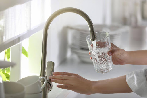 Woman filling up glass with reverse osmosis clean water from kitchen faucet