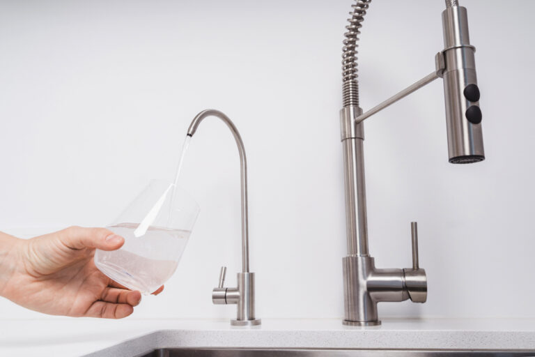 A person pouring a glass of clean, filtered well water from a point-of-use kitchen faucet